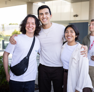 Three students at Grad Mixer event, they have their arms around each other and are smiling.